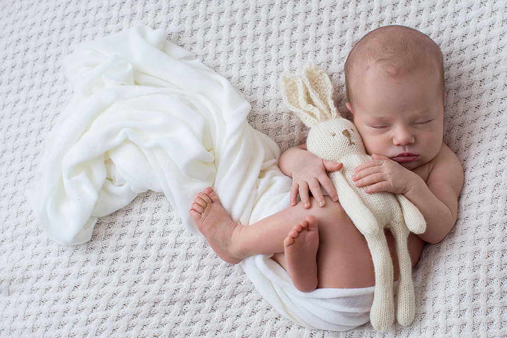 Newborn baby photographed sleeping with toy bunny.