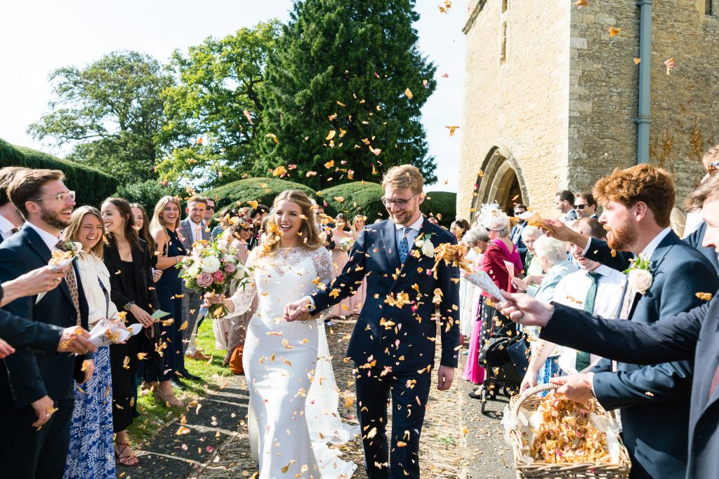Bride and groom celebrating with confetti after their wedding ceremony at All Saints Church, Turvey.
