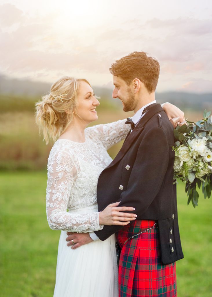 Bride and groom gazing into each other's eyes, with the bride’s bouquet draped over the groom’s shoulder, captured by Sarah Oliver at Cooling Castle Barn, Rochester.