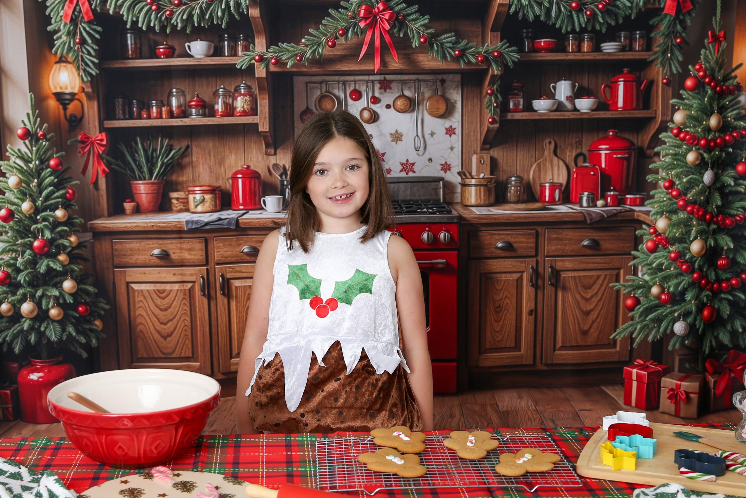 A young girl dressed in a Christmas pudding costume smiles in a festive pine kitchen decorated for the holidays. Photo by Sarah Oliver Photographer at So Studios, Epping, Essex